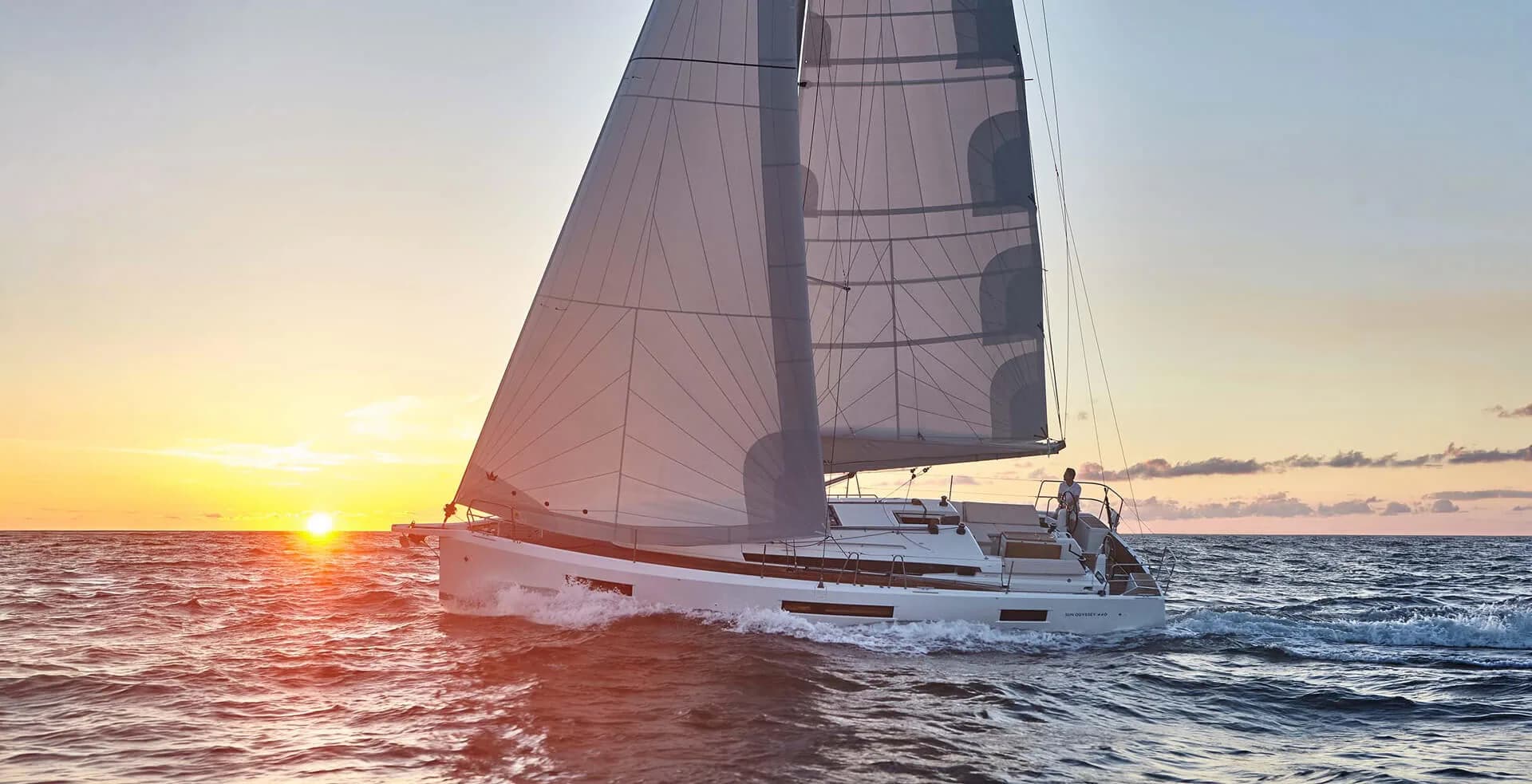 A Jeanneau sailboat under full sail at sunset