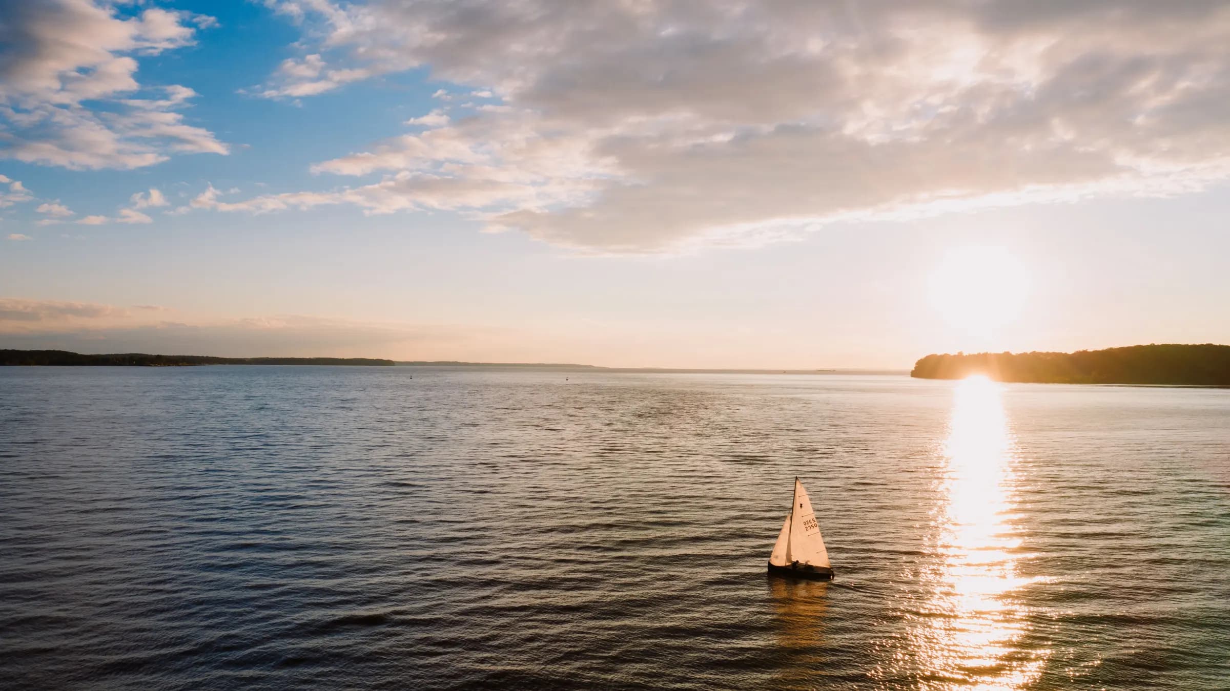 A small sailboat crossing a calm bay at sunset